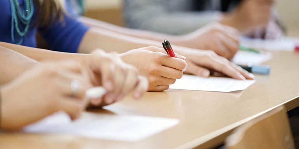 3 students holding pens and writing the exams.